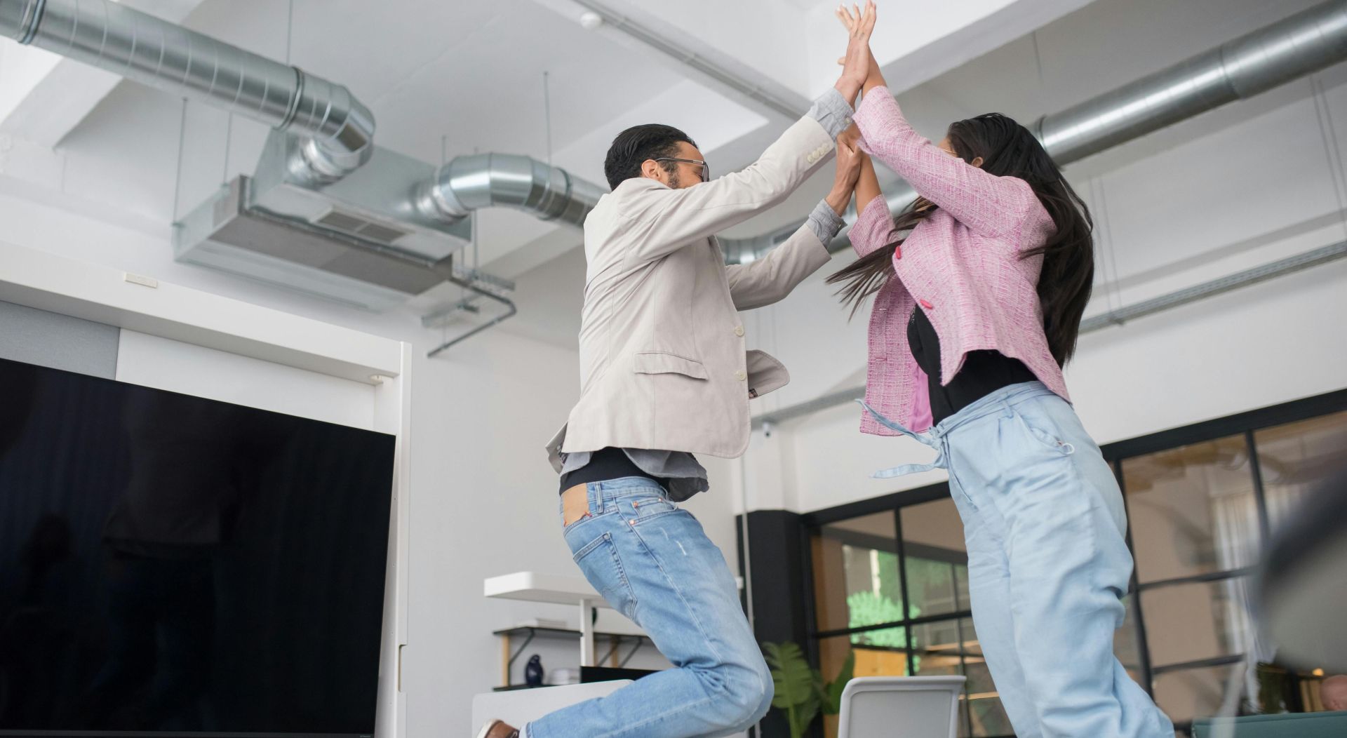 Two colleagues jumping and high-fiving in an office, symbolizing teamwork and success.
